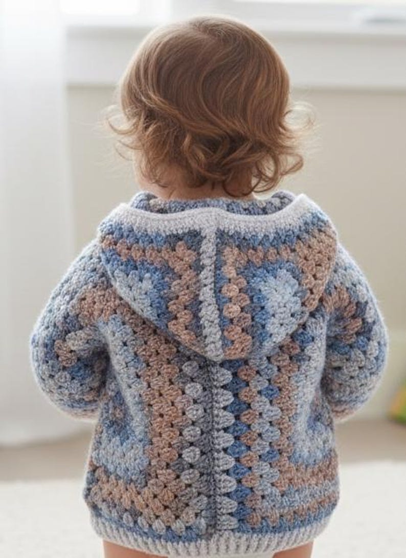 Crochet hooded baby jacket worn by baby, granny square motif body and hood, perfect handmade baby shower gift
