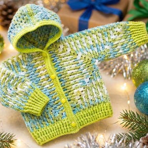 Puede incluir: Un cárdigan de bebé tejido a mano con capucha. El suéter está hecho con hilo azul, blanco y verde, con un ribete y botones de color verde brillante. La prenda acogedora es ideal para mantener a un bebé abrigado.