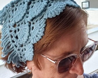 May include: A light blue crochet head covering with a leaf-like pattern. The head covering is made of a soft, textured yarn and has a scalloped edge. The head covering is worn on the head.