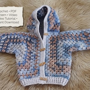 Peut inclure: Un cardigan pour bébé au crochet avec capuche, motif granny square bleu, beige et gris. Il comporte des boutons en bois et le texte "Crochet • PDF Pattern • Video Video Tutorial • Instant Download" sur une étiquette en papier.