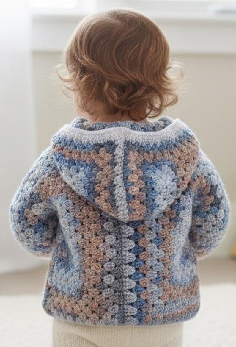 May include: A hooded crochet sweater featuring a multi-colored granny square pattern in shades of dusty blue, light grey, and muted brown. The garment has long sleeves, a hood, and a textured yarn construction with a visible stitch pattern throughout.
