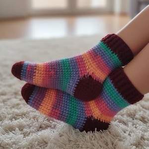 May include: A pair of colorful, handmade crochet socks. The socks feature a striped pattern in shades of pink, orange, green, and purple. The cuffs and toes are a deep burgundy color. The socks are designed to be worn.