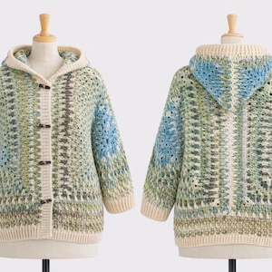 Könnte beinhalten: Handgefertigte Kapuzenjacke aus Häkelarbeit in Blau-, Grün- und Cremetönen. Die Jacke hat eine Knopfleiste vorne und eine lockere Passform. Ärmel und Kapuze sind mit cremefarbenem Garn verziert. Auf einer Büste präsentiert.