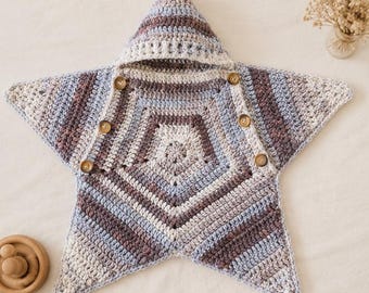 May include: A star-shaped crochet swaddle blanket featuring a hood and five wooden buttons. The textile displays a variegated pattern of cream, light blue, and muted brown yarn, constructed with a consistent stitch throughout the entire piece.