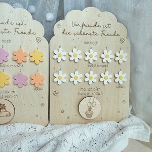 May include: Wooden countdown boards with daisy and flower cutouts. The boards have German text, including "Vorfreude ist die sch&ouml;nste Freude." One board has a car illustration, the other a cupcake with balloons.