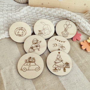 May include: A collection of seven wooden coasters with engraved illustrations. Designs include a jack-o'-lantern, a bunny with a basket, a cupcake with balloons, a person with a bag, a banner, a car with luggage, and a Christmas tree with presents.