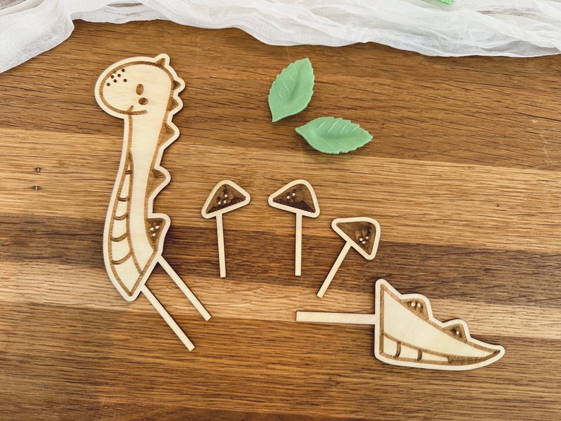 May include: Wooden craft kit featuring a dinosaur, mushrooms, and leaves. The pieces are cut out and ready to be assembled.