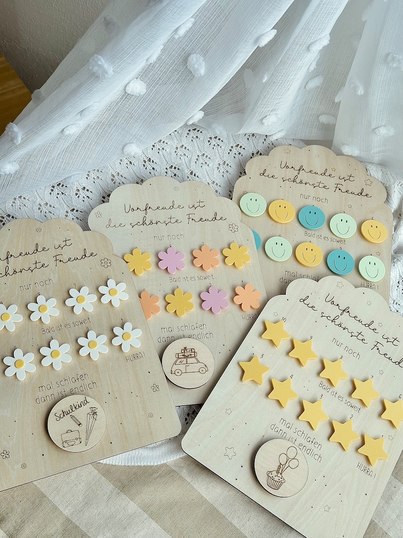 May include: Wooden plaques with various designs, including daisies, smiley faces, stars, and travel-themed illustrations. Each plaque has the German text "Vorfreude ist die sch&ouml;nste Freude" and "Bald ist es soweit."