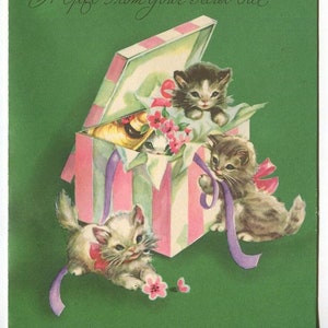 May include: A vintage greeting card with a green background featuring a pink and white striped gift box with a lid open.  Three kittens are peeking out of the box, and one is sitting on the edge of the box.  The card has the text "A Gift From Your Secret Pal" written in cursive.