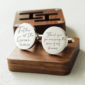 May include: Silver cufflinks with a wooden box. One cufflink says "Father of the Groom 16.08.24" and the other says "Thank you for raising the man of my dreams".