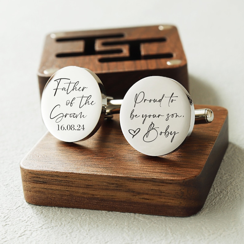 May include: Silver cufflinks in a wooden box. One cufflink says "Father of the Groom 16.08.24" and the other says "Proud to be your son, Bobby" with a heart symbol.