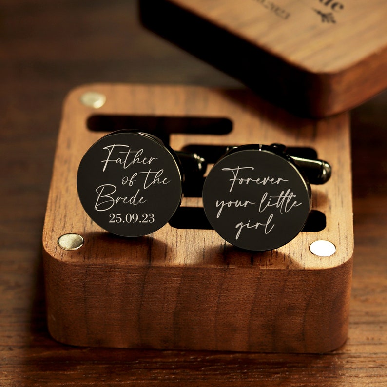 May include: Two black cufflinks in a wooden box. One cufflink says "Father of the Bride" with the date "25.09.23". The other cufflink says "Forever your little girl".