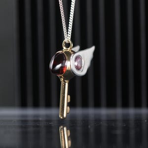 Colgante en plata de ley con forma de pico, circonitas rosa en los ojos yun granate natural como el pico del pájaro.