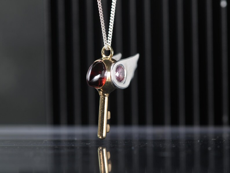 Colgante en plata de ley con forma de pico, circonitas rosa en los ojos yun granate natural como el pico del pájaro.