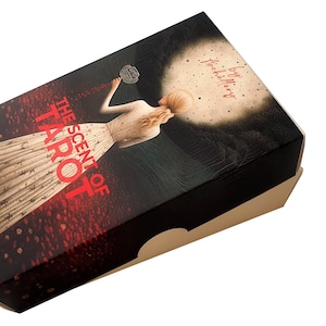 Puede incluir: Caja de la baraja de tarot "The Scent of Tarot" con fondo negro y diseño rojo y blanco. La caja muestra a una mujer con un vestido blanco con un título rojo que dice "The Scent of Tarot".