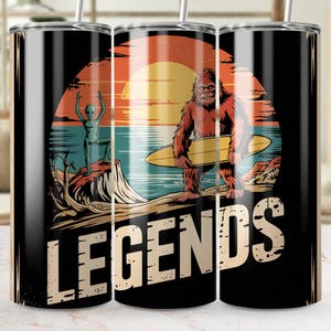 May include: Three stainless steel tumblers with a black background and colorful graphic designs. The tumblers feature an alien, a bigfoot, and a surfboard with the word "LEGENDS" printed in large white letters.
