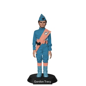 Puede incluir: Figura de Gordon Tracy, personaje de la serie Thunderbirds. Viste un uniforme azul con una banda y botas color melocotón. La base negra tiene el nombre "Gordon Tracy" impreso.