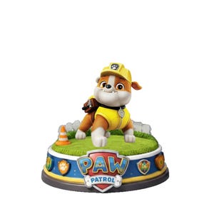 Puede incluir: Figura del personaje Rubble de Paw Patrol. Rubble, un bulldog, lleva un casco y chaleco de construcción amarillos. La figura está sobre una base con el logo de Paw Patrol y una zona de césped verde.