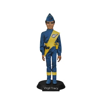 Puede incluir: Una figura de acción vintage de Virgil Tracy, de pie sobre una base negra. La figura viste un uniforme azul con detalles amarillos, incluyendo una faja y un cinturón. El sombrero y las botas de la figura son azules. La base dice "Virgil Tracy".