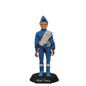 Puede incluir: Figura de acción vintage de Alan Tracy, vestido con un uniforme azul con gorra y botas a juego. La figura tiene una faja blanca y está sobre una base negra con el nombre "Alan Tracy" impreso.