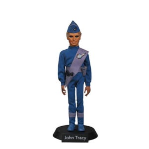 Puede incluir: Figura de acción de John Tracy, vestido con un uniforme azul y gorra a juego, con una faja gris. La figura se encuentra sobre una base negra con el nombre "John Tracy". La figura tiene el pelo rubio y está de pie.
