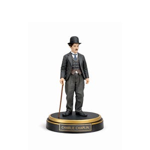 May include: A figurine of Charlie Chaplin in a black suit, bowler hat, and holding a cane. The figure stands on a black base with a gold rim and a plaque that reads "Charlie Chaplin". The figure has a painted mustache and is wearing a tie.