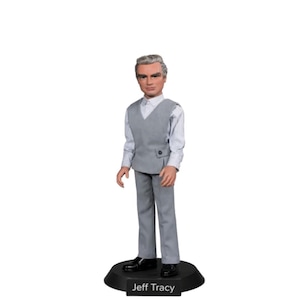 Puede incluir: Una figura de acción de Jeff Tracy con un traje gris, camisa blanca y zapatos negros. La figura está sobre una base negra con el nombre "Jeff Tracy". La figura tiene cabello gris y está de pie.