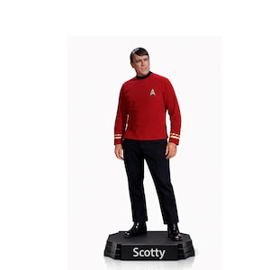 May include: A figurine of a man in a red long-sleeved top with gold detailing on the cuffs and a black collar. He wears black trousers and shoes, standing on a black base with the name "Scotty" in white. A collectible item.