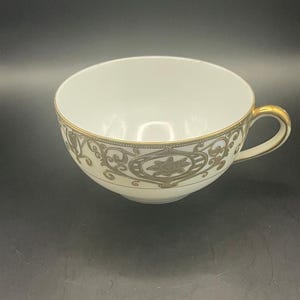 May include: A white ceramic mug with a black handle and the text "But First, Coffee" in a bold, black font. The mug is set against a blurred background, suggesting a cozy setting.