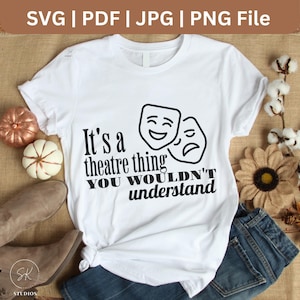 May include: White t-shirt with the text "It's a theatre thing you wouldn't understand" and two theater masks. The shirt is styled with jeans, boots, and decorative pumpkins.