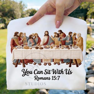 May include: White fabric with an embroidered depiction of the Last Supper. The image features figures around a table, with text that reads "You Can Sit With Us Romans 15:7 STUDIOS". The embroidery uses brown, red, and beige threads.
