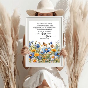 Può includere: Una stampa incorniciata con un design floreale ad acquerello, con fiori blu, gialli e bianchi e due farfalle. La stampa include il testo "Poiché io so i pensieri che ho per voi..." da Geremia 29:11.
