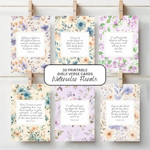 May include: Six rectangular cards featuring watercolor floral patterns in shades of purple, blue, and orange, each displaying a unique Bible verse in black script text, suspended by wooden clips on a horizontal string against a white background.