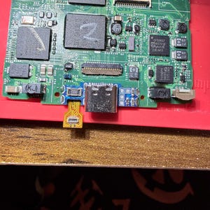 Puede incluir: Primer plano de una placa de circuito con varios componentes electr&oacute;nicos. La placa es principalmente verde con detalles en rojo y dorado. Se ve un puerto USB-C, junto con varios chips y conectores. La imagen est&aacute; bien iluminada.