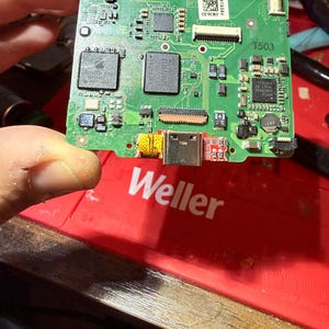 May include: A green circuit board with various electronic components, including chips, connectors, and a USB-C port. The board has the Apple logo and the text "APPLE &copy;2008 820-2437". The board is held by a person's fingers.