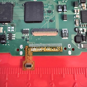 May include: A close-up of a green circuit board with various electronic components. A small, flexible circuit board labeled "iPodUSB FPC v.1.1" is connected to the main board. A red ruler is visible at the bottom, with markings in inches.