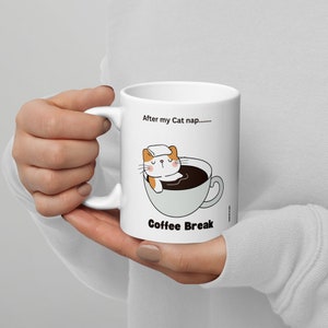 Könnte beinhalten: Weiße Keramiktasse mit einer Cartoon-Katze, die in einer Kaffeetasse schläft. Der Text auf der Tasse lautet "After my Cat nap..... Coffee Break".