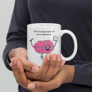 Op de afbeelding: Een witte keramische mok met een cartoonbrein dat een bril draagt en een potlood en een boek vasthoudt. Op de mok staat "Short breaks make me more effective."