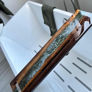 Puede incluir: Una bandeja de baño de madera con una incrustación de resina epoxi verde y blanca. La bandeja tiene un portavasos incorporado y un asa.
