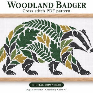 Może przedstawiać: Wzór do haftu krzyżykowego w formacie PDF zatytułowany WOODLAND BADGER przedstawiający sylwetkę borsuka złożoną z zielonych i żółtych liści paproci oraz czarnych pasków. Wzór jest umieszczony w jasnej drewnianej ramie z napisem DIGITAL DOWNLOAD.