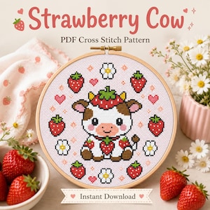 May include: A circular wooden embroidery hoop containing a cross stitch pattern of a white and brown cow wearing a strawberry hat, surrounded by strawberries, flowers, and hearts on light pink fabric. The text reads Strawberry Cow PDF Cross Stitch Pattern.