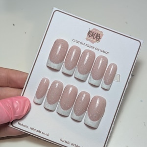 Könnte beinhalten: Ein Set individueller Press-On-Nägel mit French-Tip-Design. Die Nägel sind hellrosa mit glitzerndem Finish und weißen Spitzen. Auf der Karte steht "RKB CUSTOM PRESS ON NAILS" mit Website- und Social-Media-Informationen.