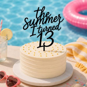 May include: A black cake topper with the text "the Summer I turned 13" in a cursive font, positioned on a round white frosted cake decorated with small yellow dots. The cake sits on a white plate, with a pool and pool accessories in the background.