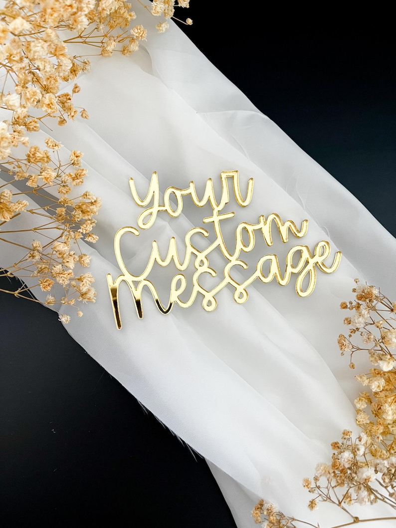 K&ouml;nnte beinhalten: Ein goldfarbenes Acrylschild mit dem kursiven Text "Your Custom Message" in einer reflektierenden, metallischen Oberfl&auml;che. Der Schriftzug ist aus einem St&uuml;ck gefertigt und weist eine glatte, gl&auml;nzende Oberfl&auml;che auf, die das Licht reflektiert.