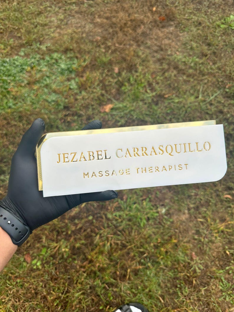 Pu&ograve; includere: Un cartello bianco con lettere dorate che recita "Jezabel Carrasquillo Massage Therapist".