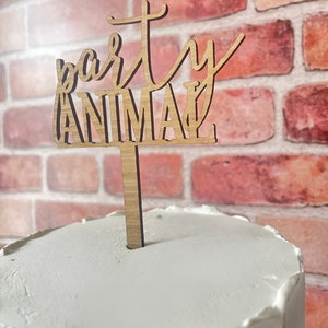 Pode incluir: Um topo de bolo de madeira com as palavras "party animal" em fonte cursiva. O topo está em um bolo branco.