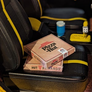 May include: Two Pizza Hut pizza boxes stacked on top of each other. The top box has the words "Pizza Hut" and "Rewards" printed on it. The bottom box has the words "Hut Rewards" printed on it.