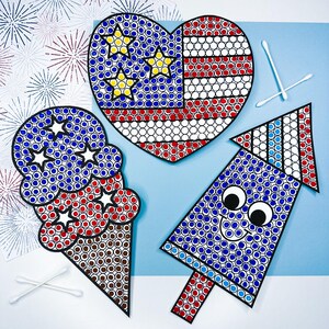 May include: A heart-shaped cutout with a red, white, and blue star-spangled pattern, an ice cream cone cutout with white stars, and a rocket cutout with googly eyes, all featuring dot-art designs alongside two white cotton swabs.