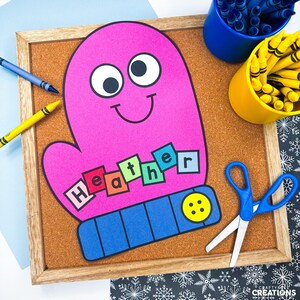 Op de afbeelding: Een roze wantvormig knutselwerk met de naam "Heather" in kleurrijke letters gespeld. De want heeft een lachend gezicht en wordt weergegeven op een prikbord met kleurpotloden, een schaar en een houten frame. Een leuk, creatief knutselproject.