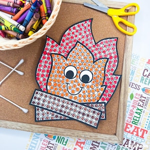 May include: A paper craft of a campfire with a smiling face, created using dot markers in red, orange, and brown. The flame is filled with red and orange dots, while the logs are filled with brown dots. It features two large googly eyes.